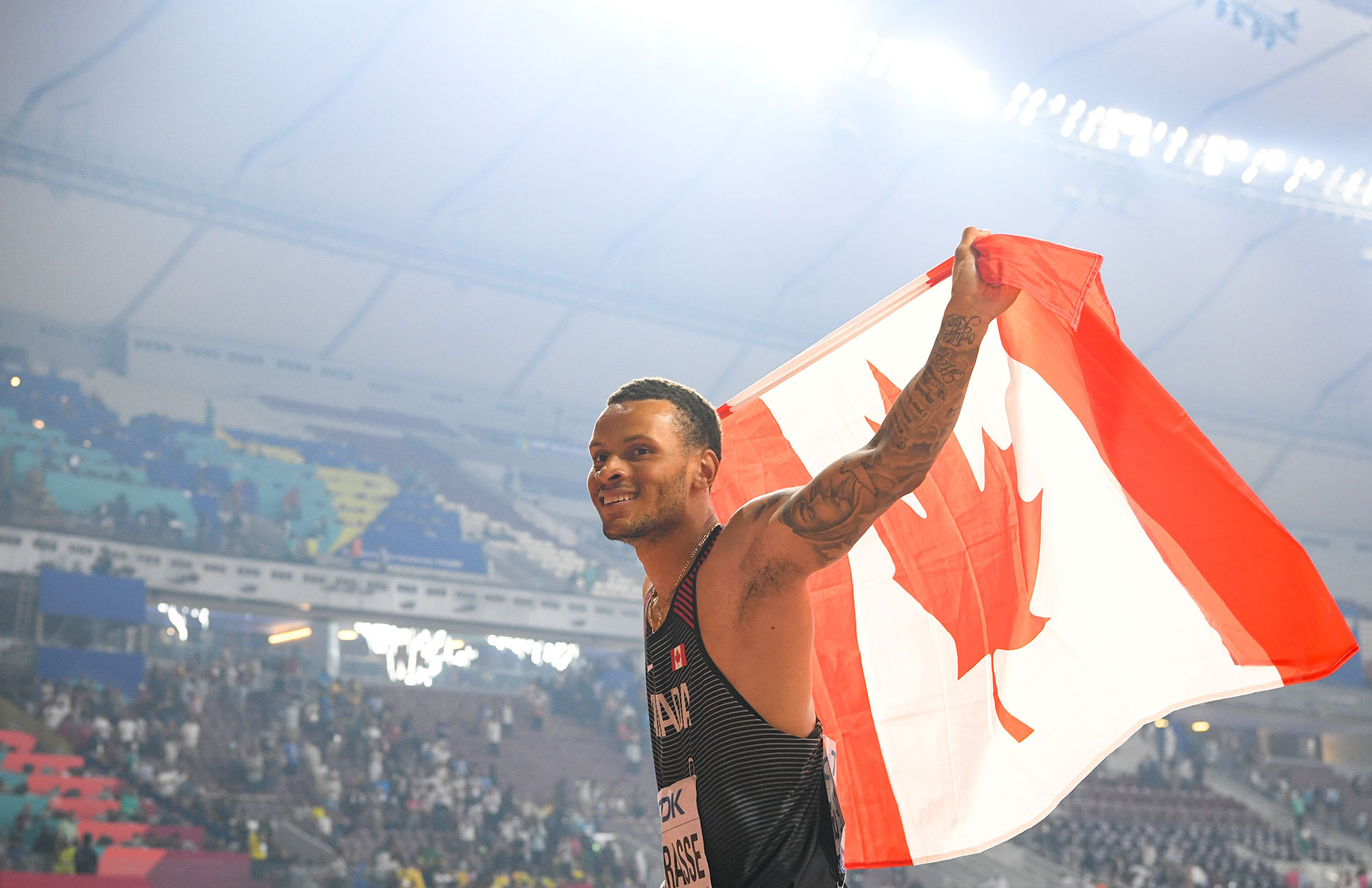 Andre De Grasse carries the Canadian flag after a race