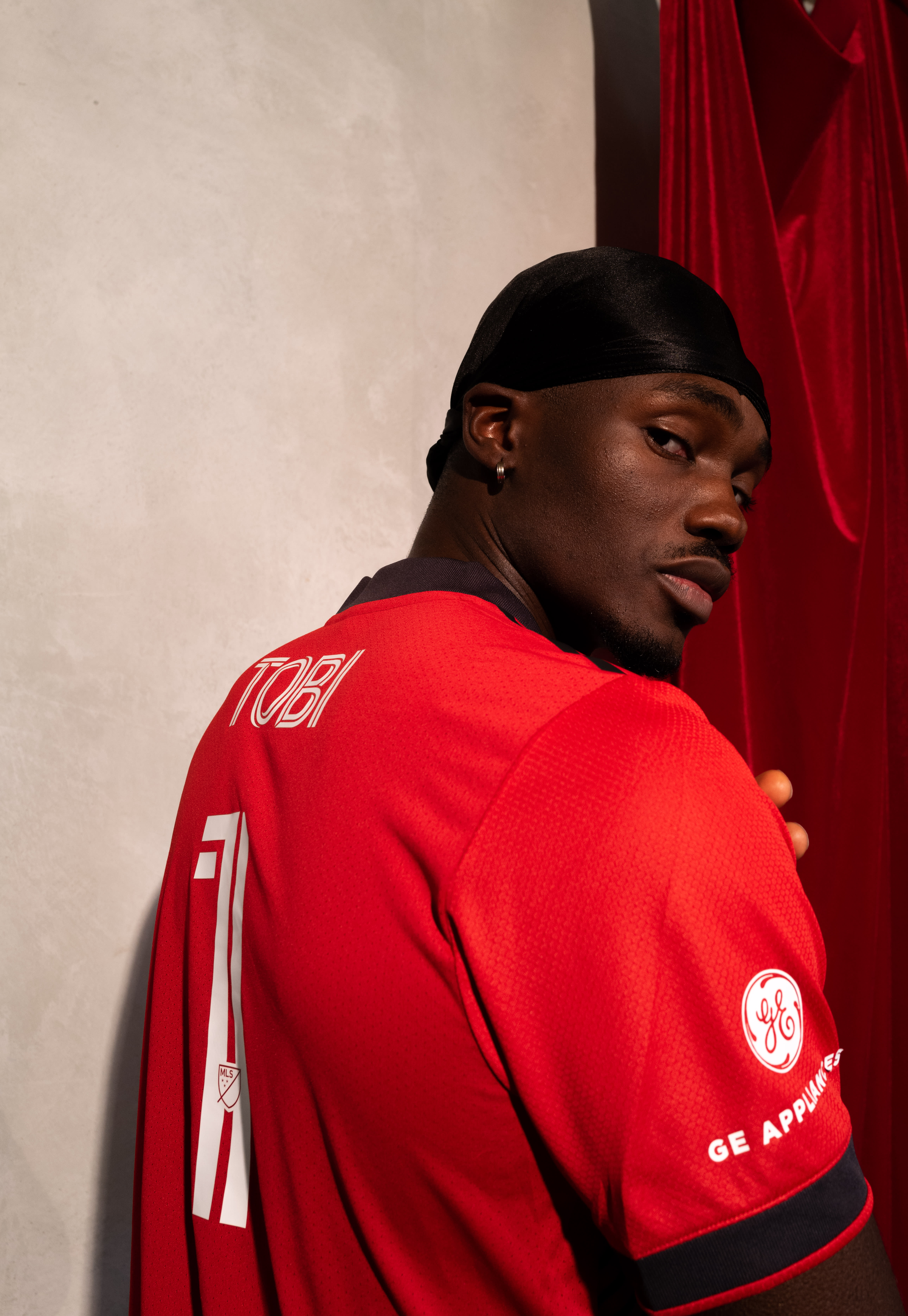 Tobi posting in a red Toronto FC jersey from the back looking over his shoulder