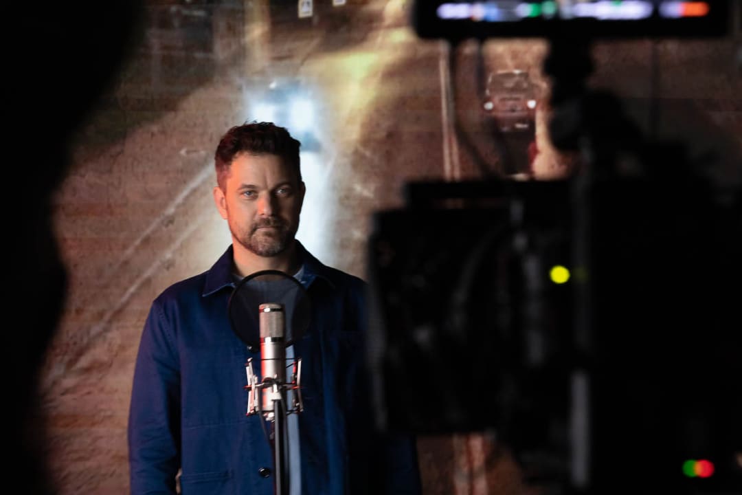 Joshua Jackson speaking into a mic, looking at a camera