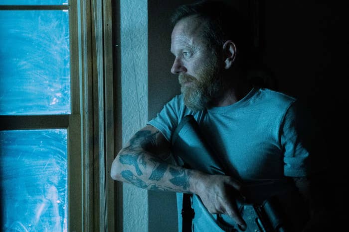 Kiefer Sutherland holding a gun, looking out a window