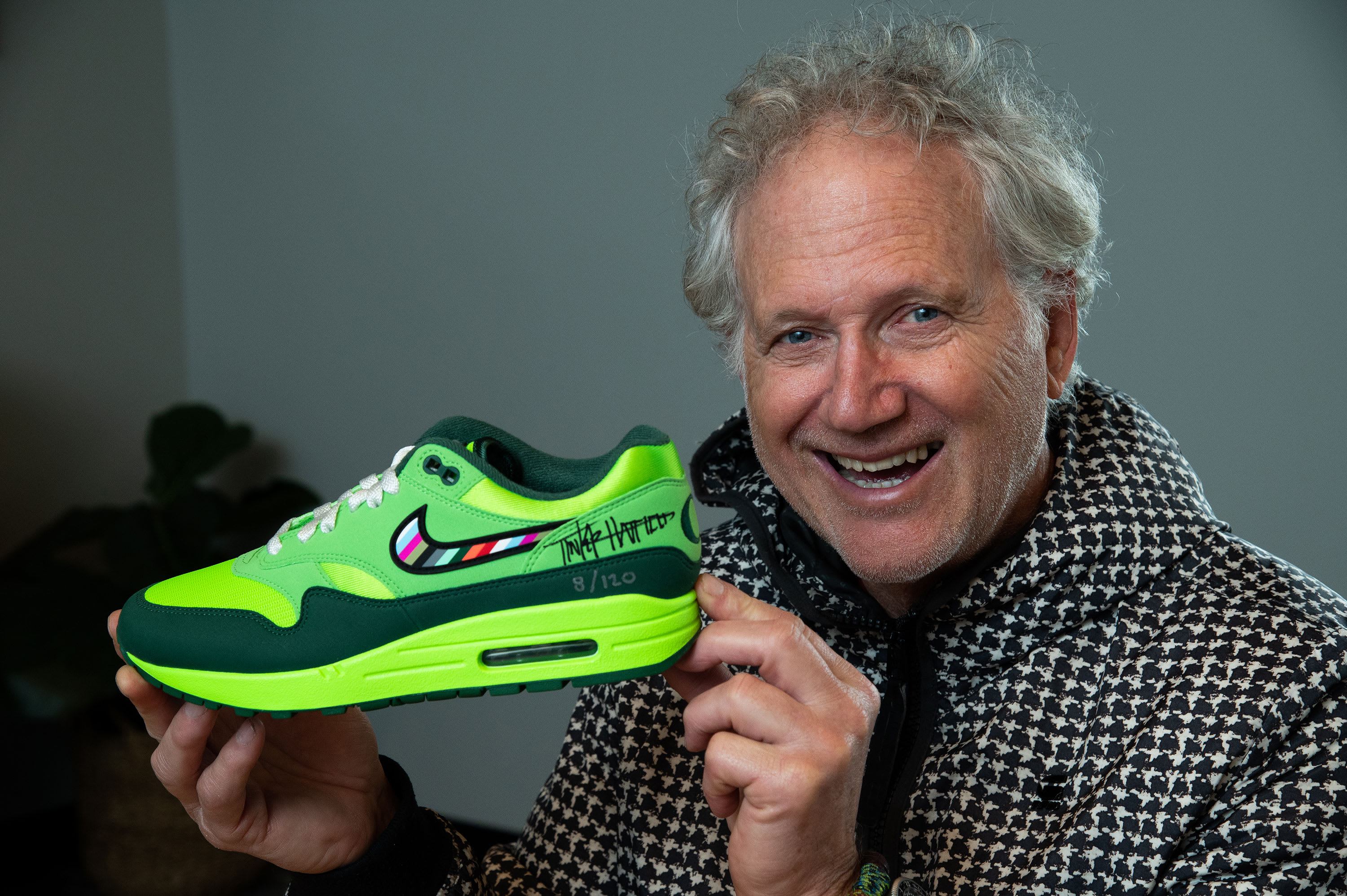 Nike designer Tinker Hatfield smiling and holding a green pair of the Division Street Air Max 1s made for Oregon Ducks athletes