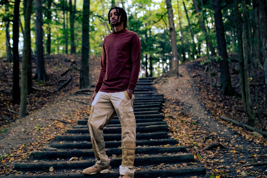 Kofi standing in a wooded area, wearing a red crewneck and khaki coloured pants