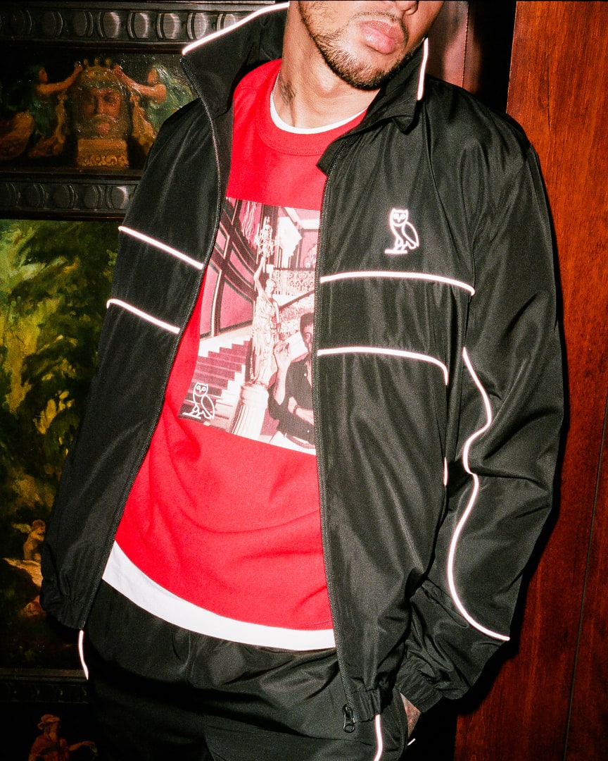 Model wearing a red crewneck featuring Tony Montana (Al Pacino) smoking a cigar, with a black OVO branded windbreaker overtop.