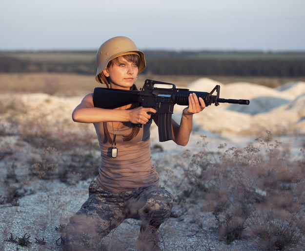 Young beautiful female soldier dressed in a camouflage with a gun