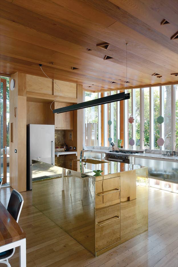 This gourmet kitchen sits inside a tiny New Zealand home, making use of a reflective island and translucent cabinets to keep things feeling open and bright.