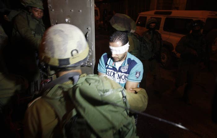 Israeli soldiers detain a blindfolded Palestinian in the West Bank City of Hebron, July 2, 2014.