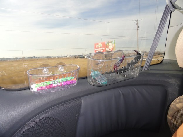 Shower caddies attached to a van windshield holding art and entertainment supplies for kids