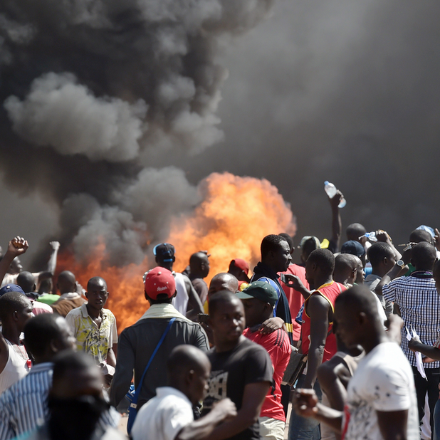 People stand in front of smoke rising from the Burkina Faso&#x27;s Parliament.