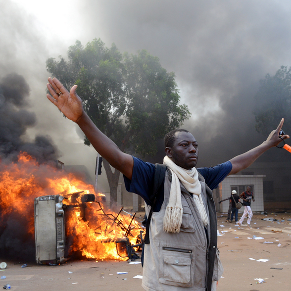 A man stands in front of a burning car near Burkina Faso&#x27;s parliament in Ouagadougou.