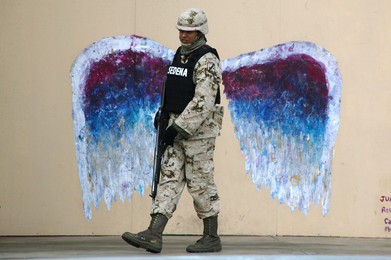 A soldier walks past graffiti depicting angel wings by artist Colette Miller in Ciudad Juarez March 18, 2015.