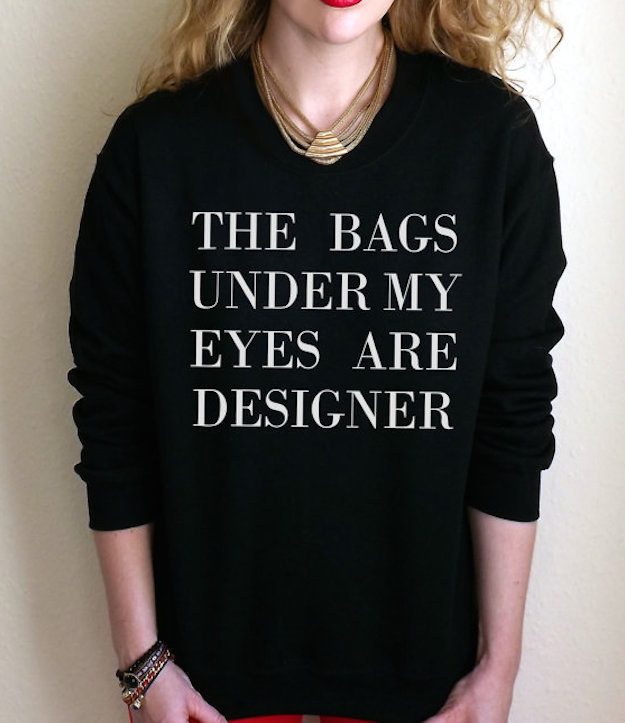 Woman of fair skin wearing a sweatshirt that says the bags under my eyes are designer