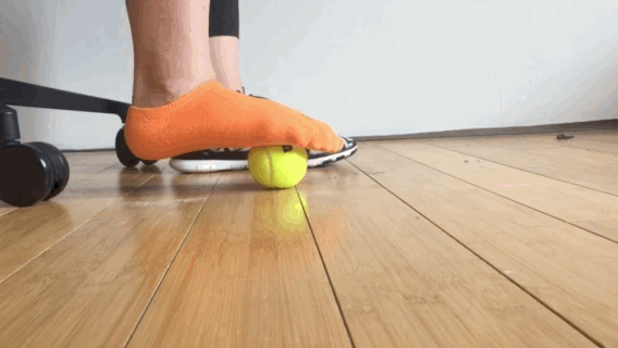 The best part about this move is you can do it under your desk without interrupting whatever you're doing. You can use a regular tennis ball, but Silbar recommends a spiked ball like this one, which will leave you feeling airy on your feet. Here's how to do it: 1. While sitting, step on the ball with a bare or socked foot and roll back and forth from heel to toe with firm pressure — but don't try to flatten the ball completely. 2. If anywhere feels particularly painful or tender, work those knots out by rolling in small circles. If you need more pressure: Do while standing instead of sitting.