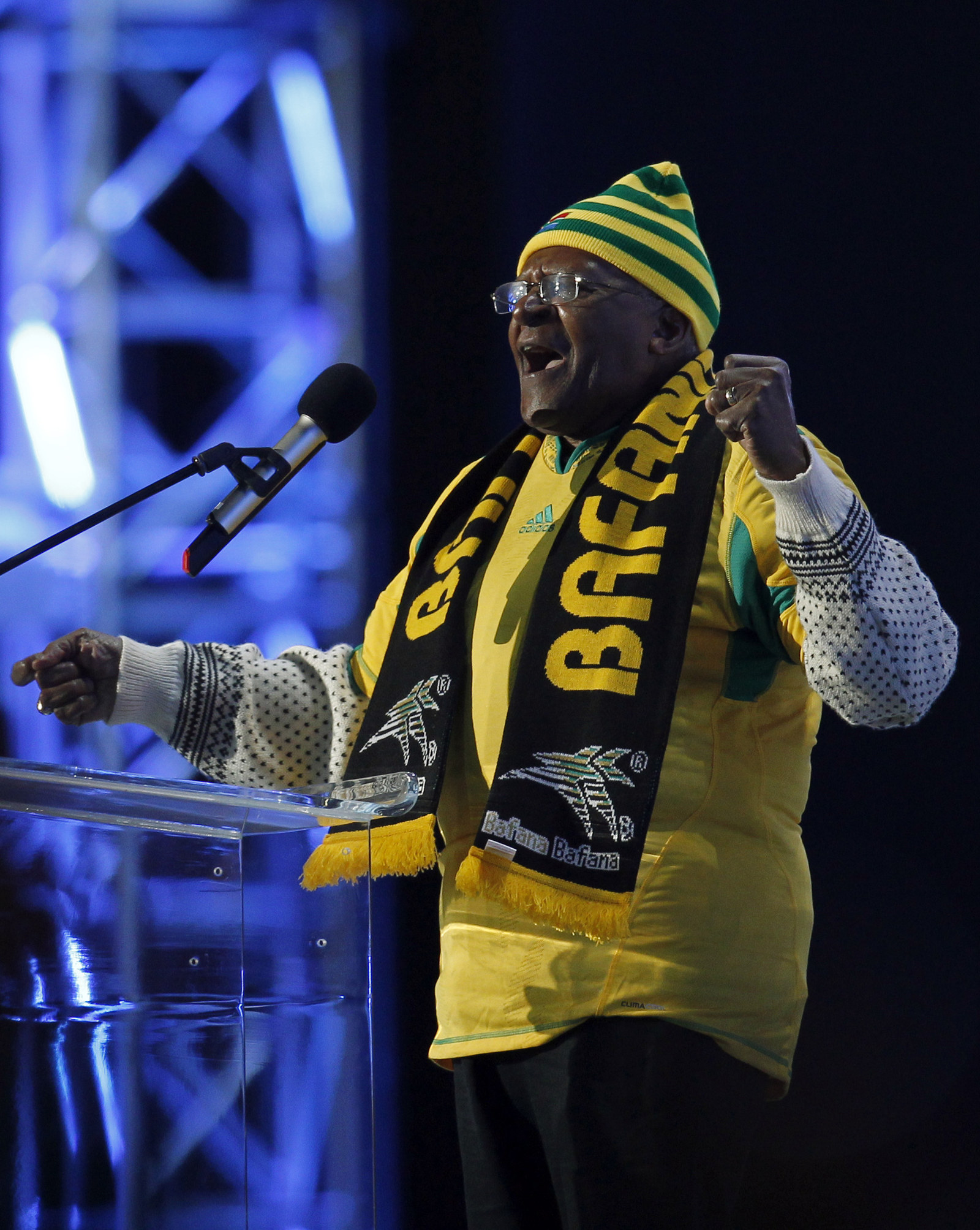 Tutu standing at a podium wearing a World Cup scarf around his neck and with his fist raised