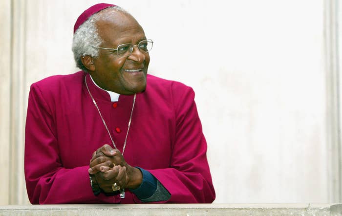 A smiling Desmond Tutu sits with hands clasped