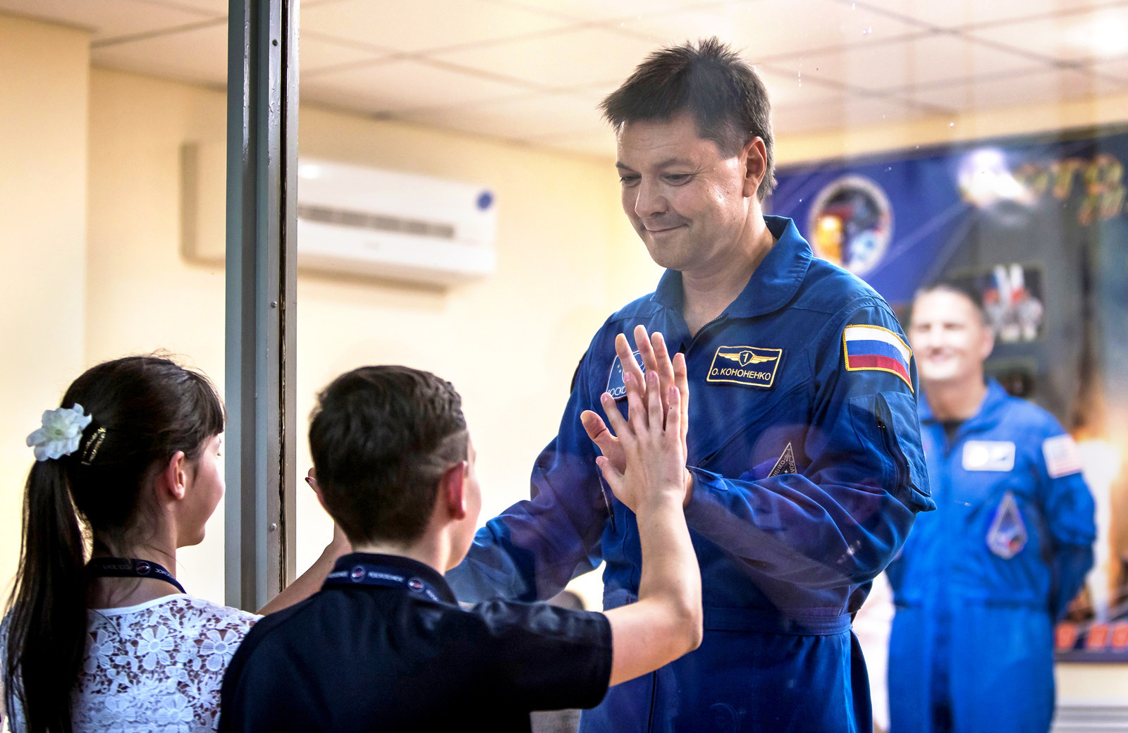 The International Space Station crew member Oleg Kononenko of Russia interacts with his children as he stands behind a glass wall at a news conference at the Baikonur cosmodrome in Baikonur, Kazakhstan.