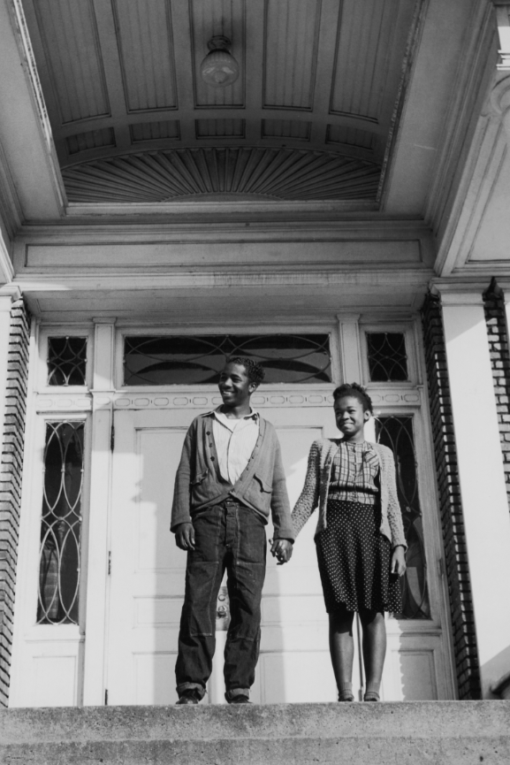 Una pareja de adolescentes se toma de las manos en el porche de una gran casa. EE. UU., alrededor de 1955.