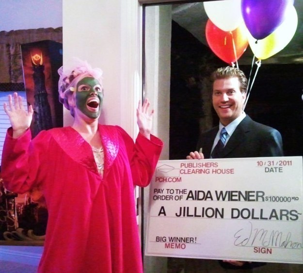 One person wearing a robe and ace mask and one man in a suit with a giant check and balloons