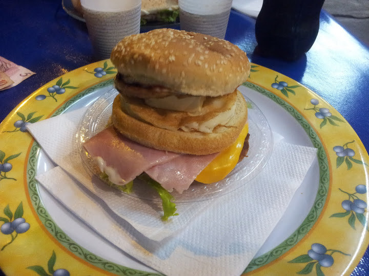 O lanche é construído com pão com gergelim, dois hambúrgueres, ovo, queijo, presunto, bacon, alface e, pasmem, POLENGUINHO.