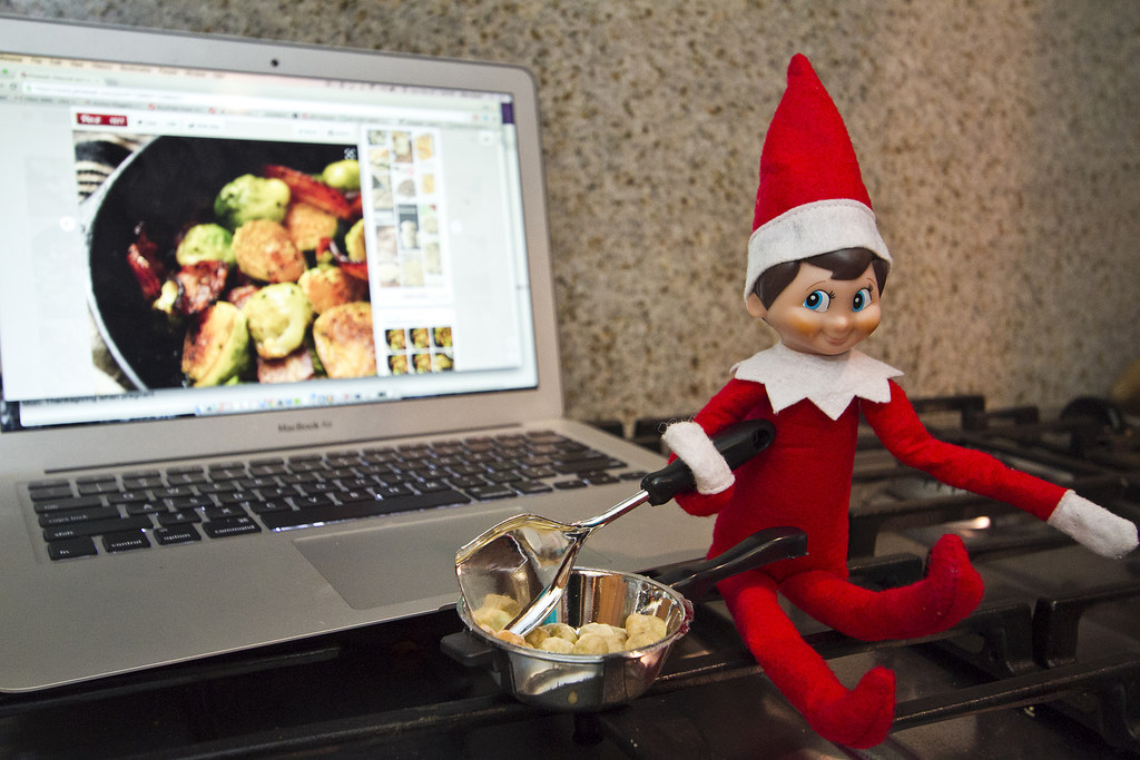 An elf sitting by a laptop preparing a dish that he sees on the screen