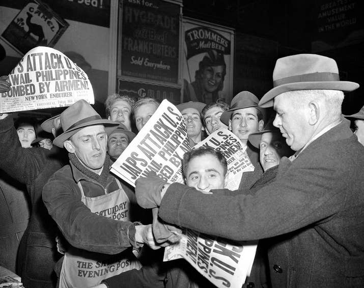 In the streets, people buy newspapers reporting the Japanese attack on U.S. bases in the Pacific Ocean.