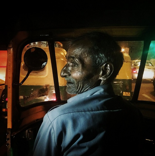 An elderly auto-rickshaw driver looks on as people celebrate the festival of Dussehra.