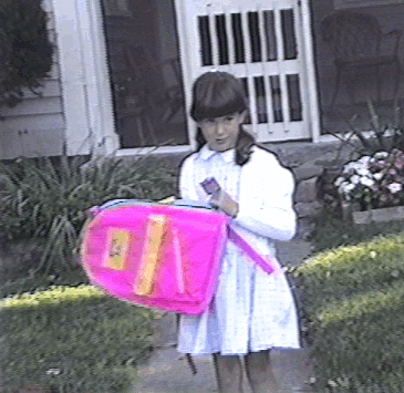 "Here I am, in all of my giant-banged glory looking like a pilgrim with my cardigan and bright pink backpack as I waited for the bus on the first day of school. I think this was first grade? The glasses came later, but the bangs ...those were in full force from a very early age. Zooey Deschanel, eat your heart out."
