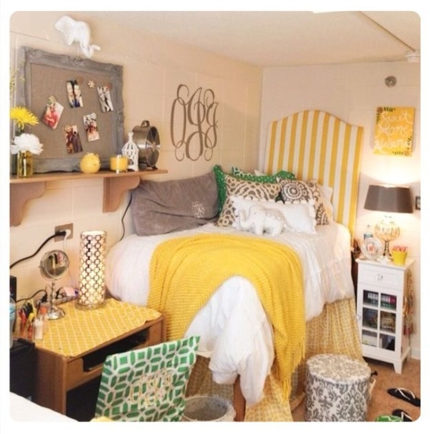 A warm, golden room with a poster board, small end tables, and a bed with a sham, throw, many pillows, and stuffed elephant
