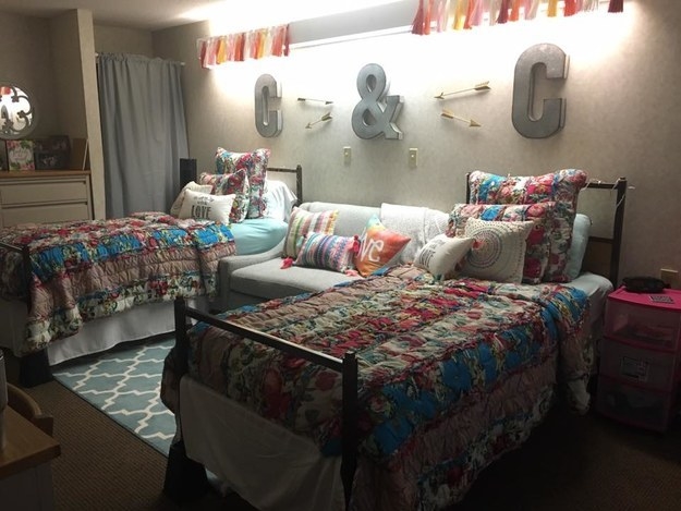 Two twin beds with colorful quilts with a chair between them and many pillows on all three