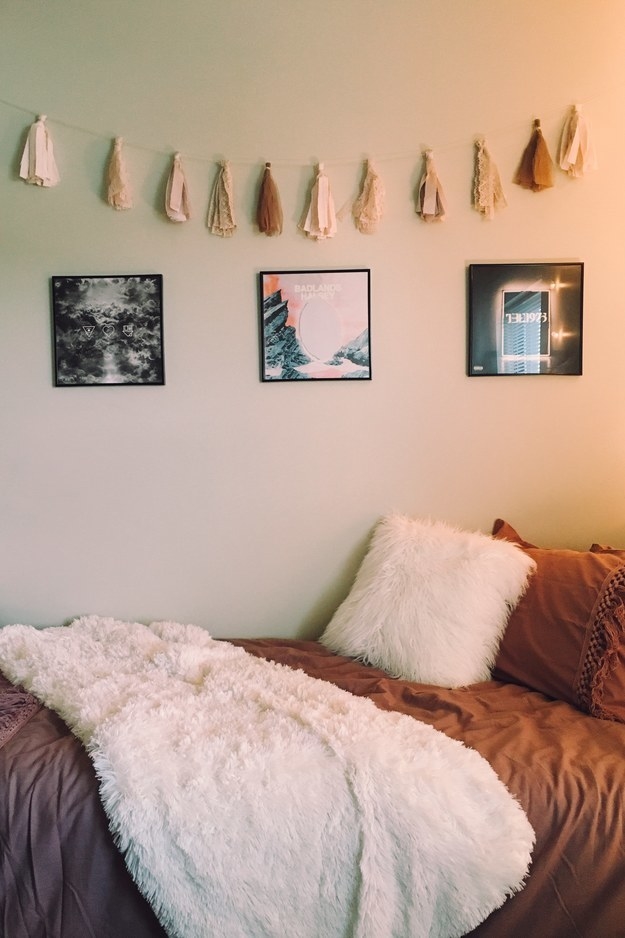 Three small framed posters and hanging decorations above a bed with a furry throw and pillow