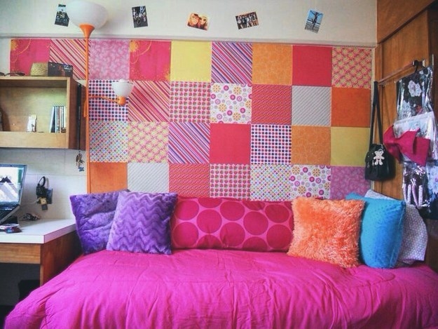 A wall with colorblock textile squares above a bed with a bright comforter and colorful pillows