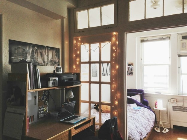 A bed and desk separated by a half glass door with fairy lights