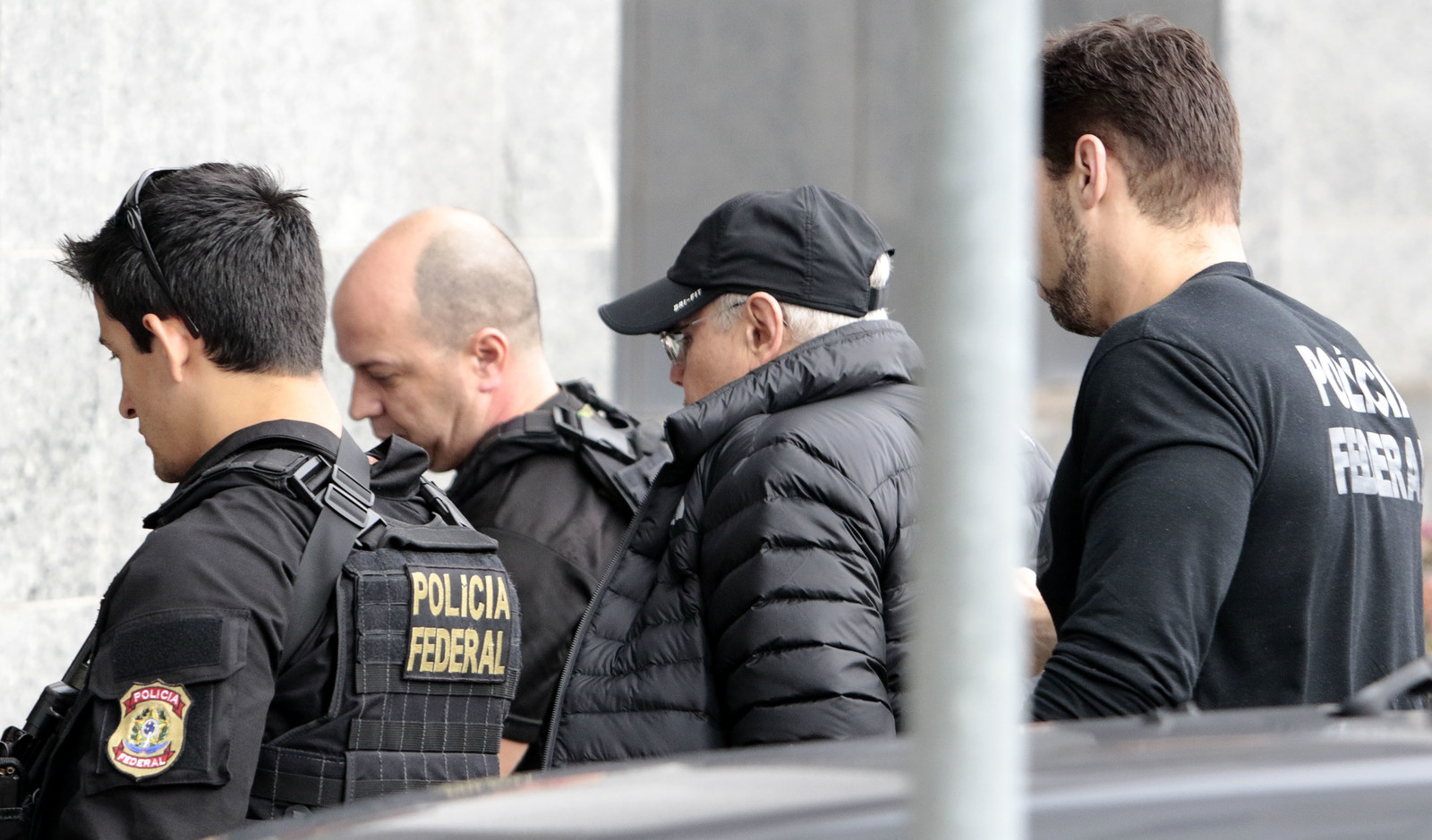 Escoltado por agentes, ex-ministro Guido Mantega (de boné) chega à Polícia Federal em São Paulo.