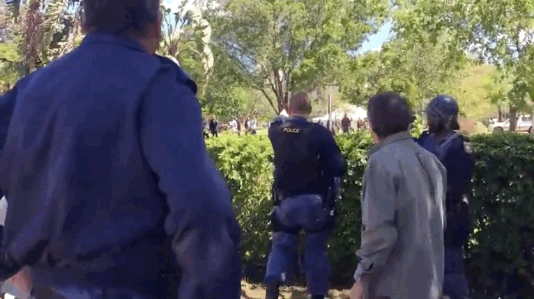 Protests have been banned on Rhodes' campus for the last several months, after a different protest movement — this one against rape culture at the university — resulted in an interdiction against demonstrations, banning students from blocking roads, disrupting classes, and other actions.That in turn has given the police the responsibility to disperse protests and arrest offenders. At one point in the video, a police officer can be heard telling a group of students on campus grounds moving towards the sidewalk where the police had gathered "Get back! Get back or I will shoot you!"