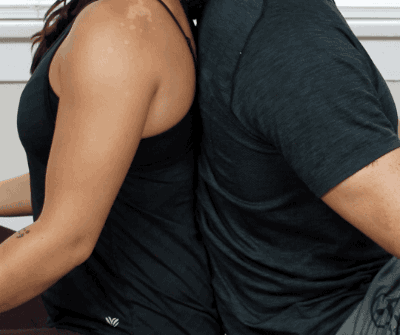 Sit cross-legged with your backs against each other. As you inhale and exhale, align your breathing patterns with your partner.