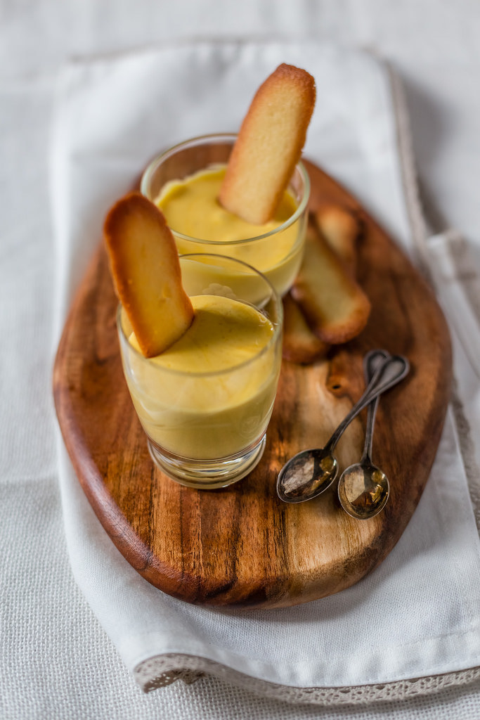 Two tiny glass cups are filled with creamy zabaglione and topped with a thin biscotti piece