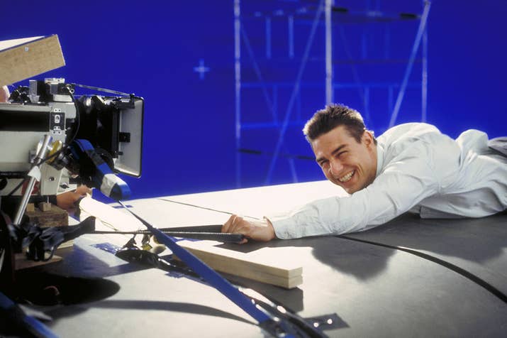 Tom Cruise as Ethan Hunt, filming a scene for the movie Mission: Impossible in a studio. In this scene, he clings to a replica of a TGV train built on the set, against a blue screen.
