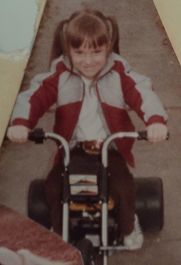 A young girl with pigtails wearing a jacket and riding a bicycle