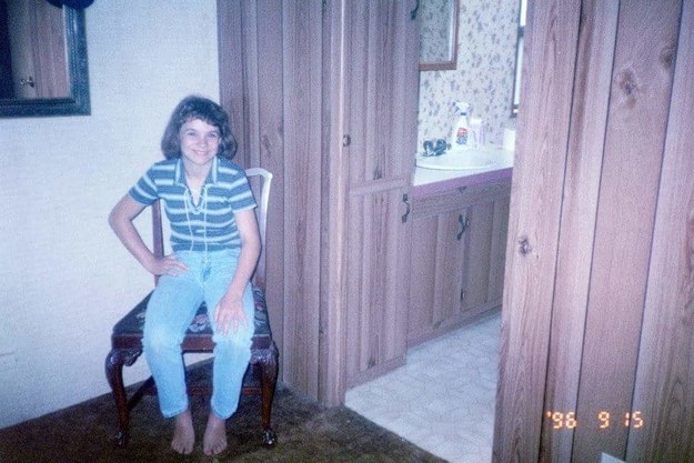 A smiling girl wearing jeans and a striped shirt and sitting by a doorway