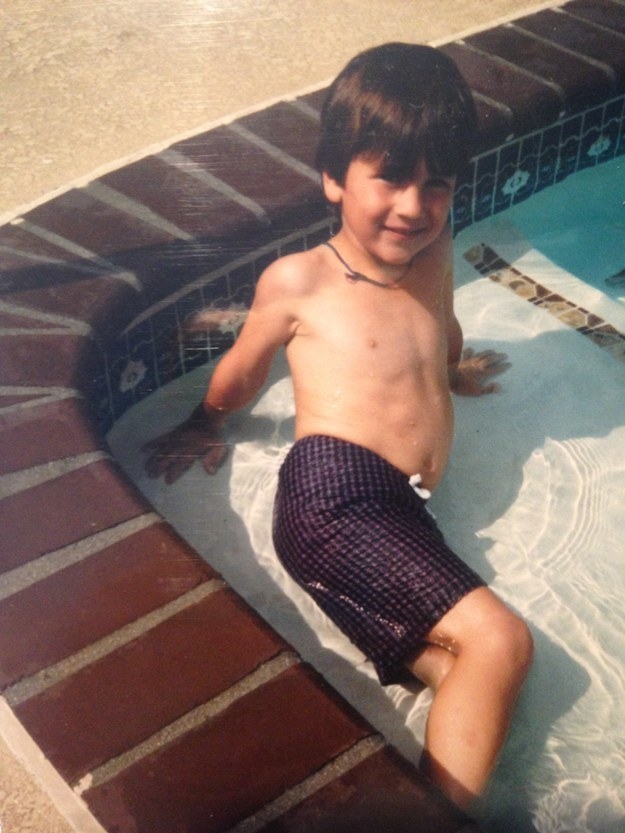 A young boy in swim trunks posing on his side in a shallow pool