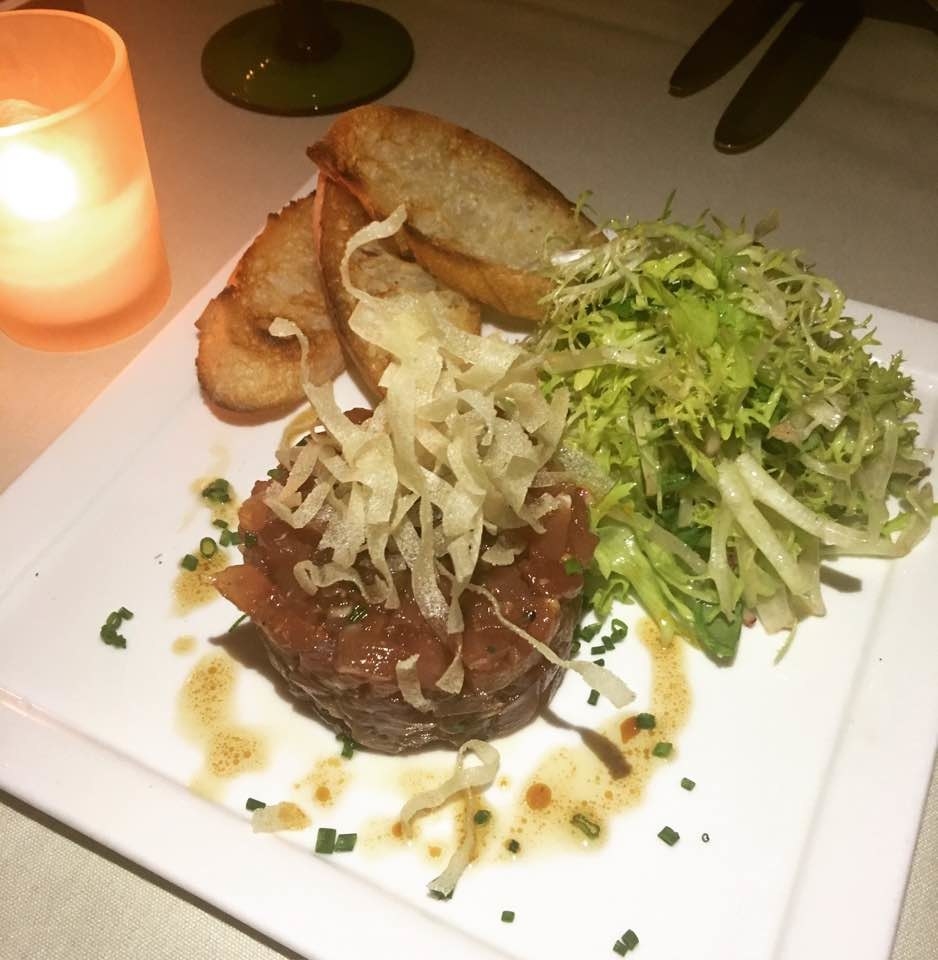 The fresh yellowfin tuna is seasoned with soy, ginger, and sesame oil and topped with crispy chips, a side of frisee salad, and toasted baguette.