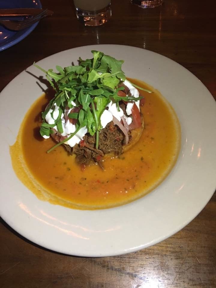On top of crunchy, crispy sweet yellow corn cake is a generous serving of tender, braised short rib. The delicious arepa is finished off with sour cream, pickled onions, tomatoes, and arugula.