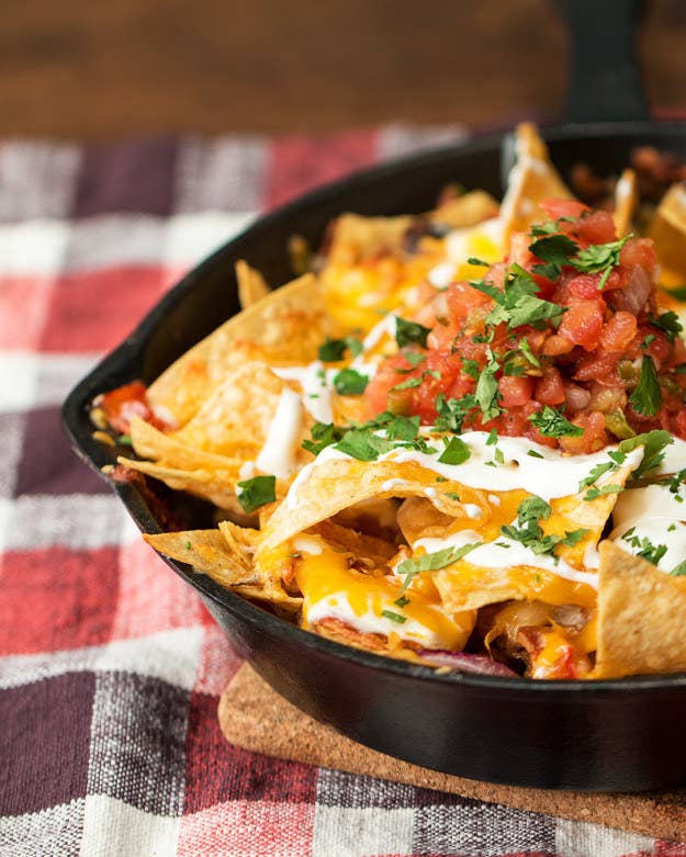 cast iron pan full of nachos with toppings like red onions and cheese