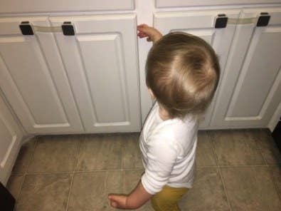 reviewer&#x27;s pic of a toddler unable to get into a cabinet thanks to door locks