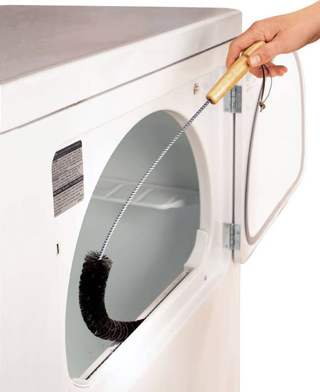 person using long brush to clean out the lint trap in a front-load clothes dryer