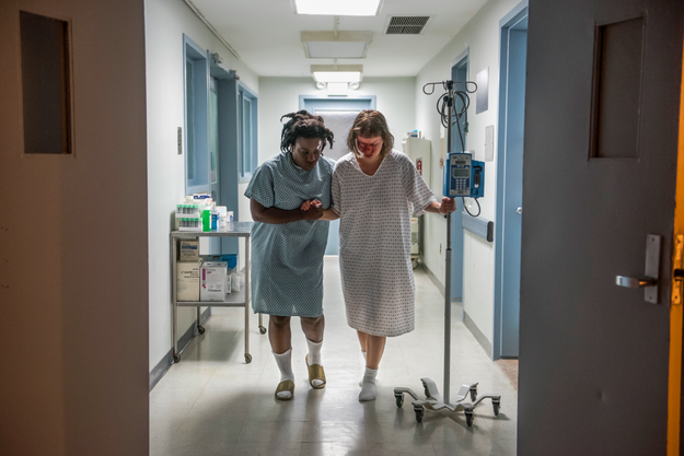 Suzanne walking Maureen through what looks like a hospital wing.
