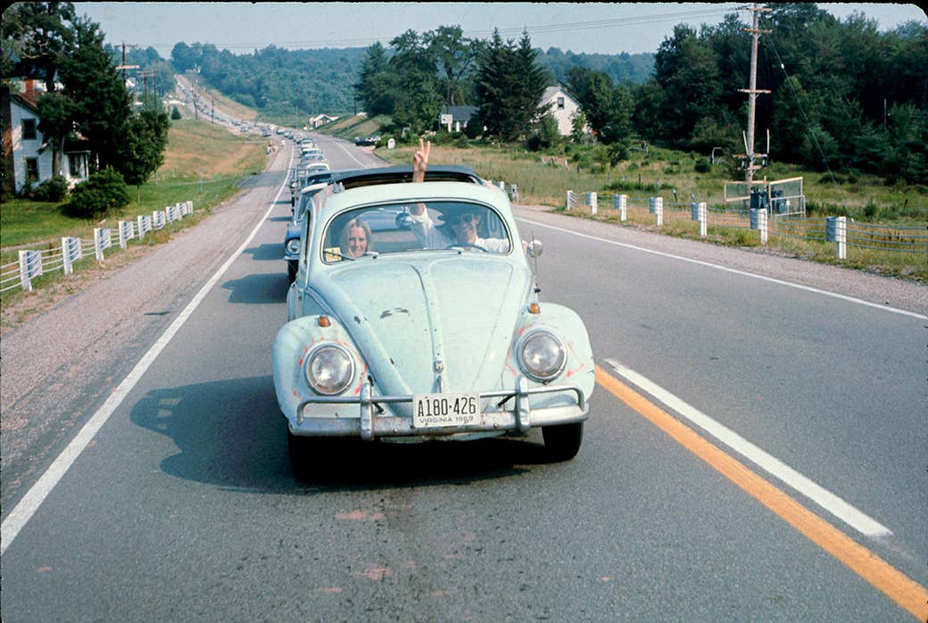 Um homem que conduz um besouro de Volkswagen faz sua maneira à música de Woodstock e à feira das artes enquanto ilumina um sinal da paz através do sunroof em 1969.