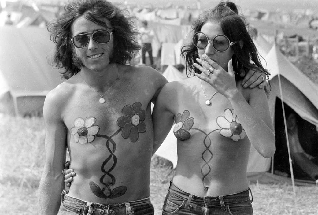 Um par com pintura de corpo de harmonização da flor anda junto durante a ilha do festival do Wight no Reino Unido em 1970.