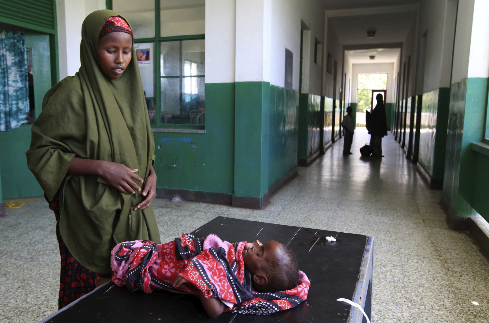 A Somali woman attends to her malnourished child along a corridor of the pa...