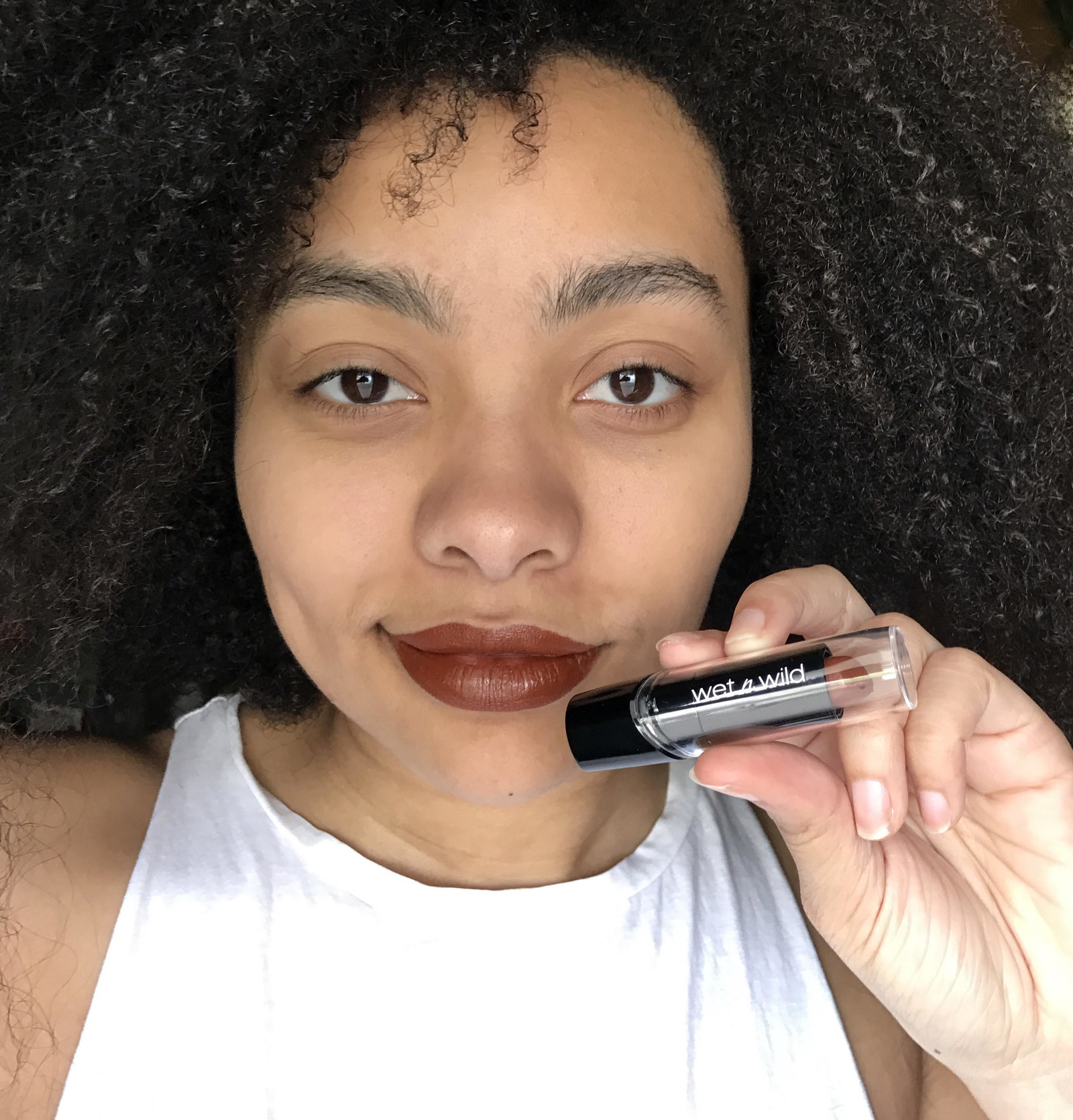 A person holding a tube of the wet n wild lipstick by their mouth