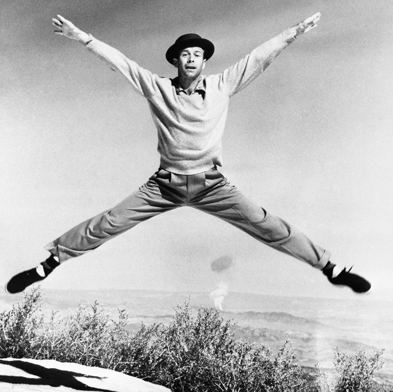 Dancer Gene Nelson performs what he calls the 'Atom Antic' on a mountaintop near Las Vegas, with a real atomic mushroom rising in the background.